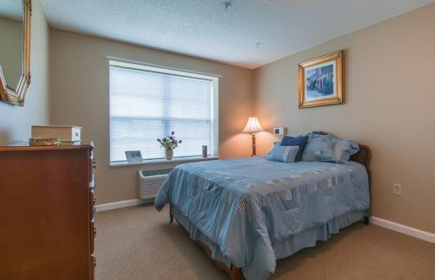 A cozy bedroom with a neatly made bed, a bedside lamp, and a window with blinds.