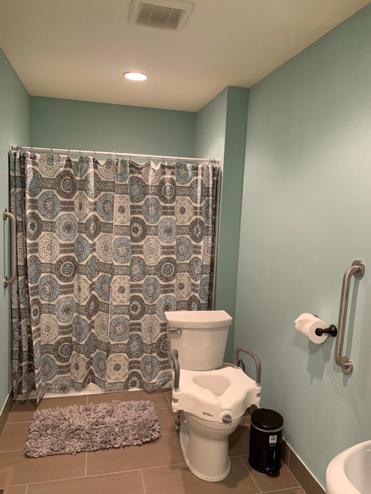 A bathroom with light blue walls featuring a toilet and a shower with a patterned curtain.