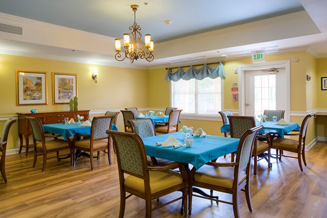 A well-lit dining room with tables set for meals, featuring elegant chandeliers and blue tablecloths.