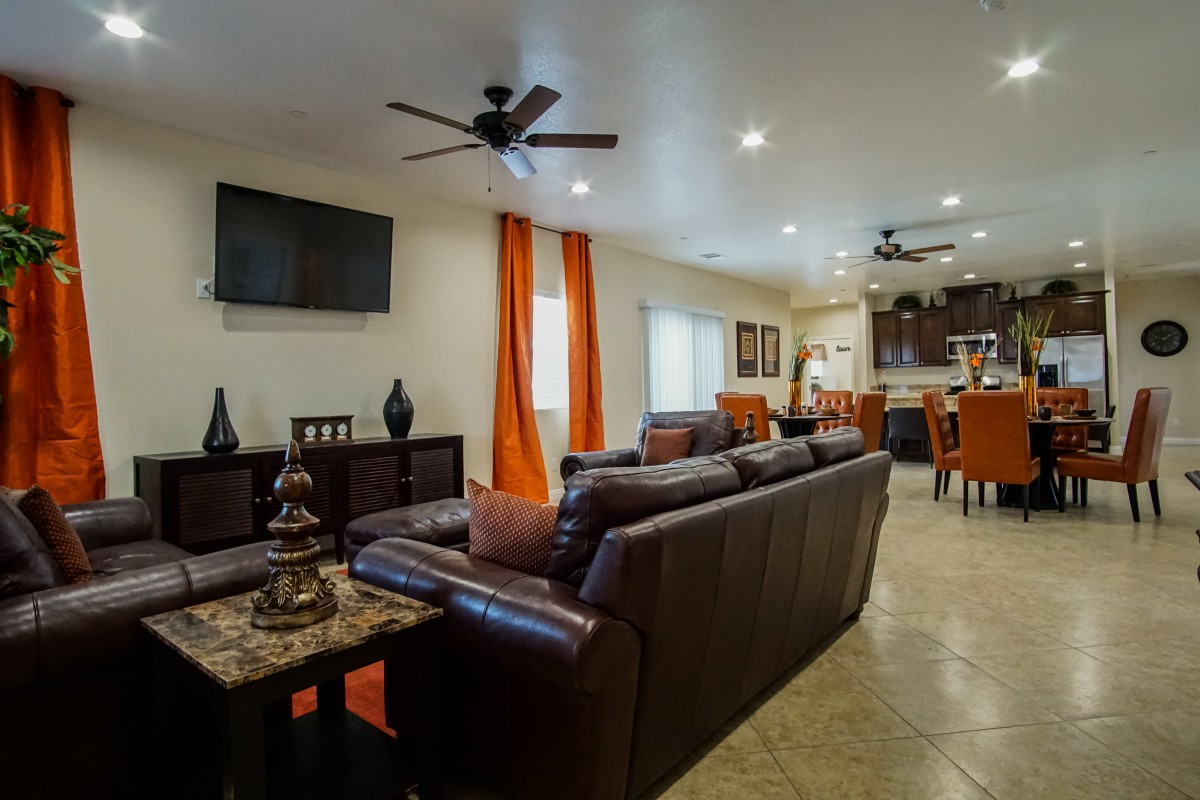 A modern living room with a cozy arrangement featuring a large couch, ceiling fans, and bright orange curtains.
