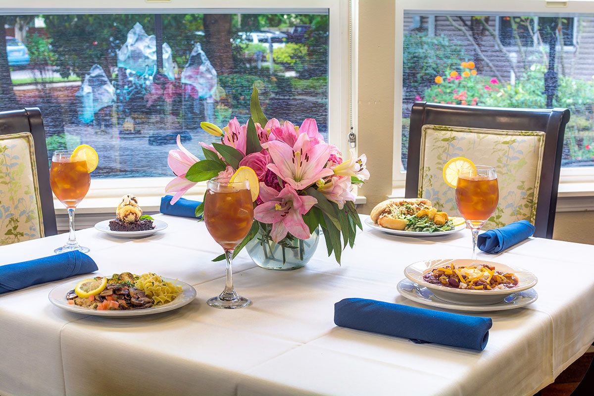 A beautifully set dining table with floral centerpiece, various dishes, and iced tea by a window.