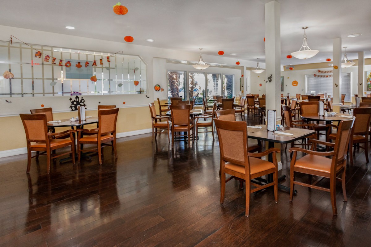 A well-lit dining area with neatly arranged tables and chairs, featuring warm decor and modern lighting.