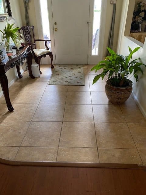 An entryway with tile flooring, decorated with a potted plant and wooden furniture.