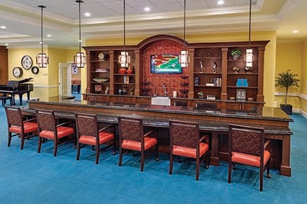 A modern lounge area with a bar-style seating arrangement, featuring bookshelves and pendant lighting.