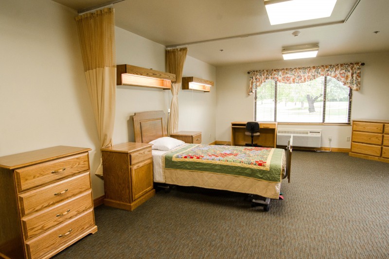 A clean and orderly hospital room with a single bed and wooden furniture.