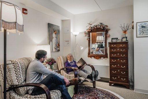 A cozy living room where a young man engages in conversation with an elderly woman, surrounded by warm decor.