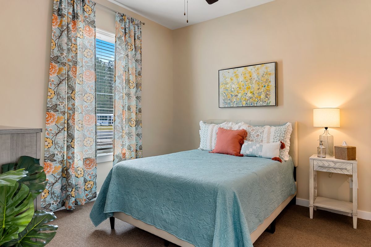 A cozy bedroom with a neatly made bed, colorful curtains, and a bright painting on the wall.