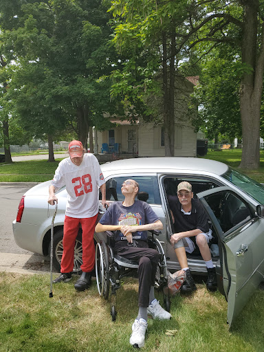 A group of friends enjoying a sunny day outside with a car and wheelchair.