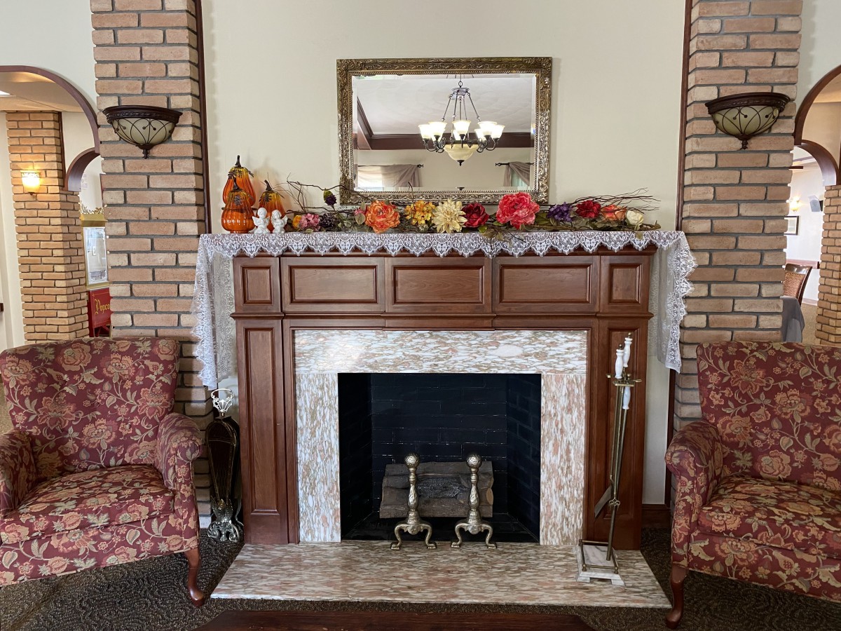A cozy indoor fireplace with autumn decorations on the mantel, flanked by two armchairs.