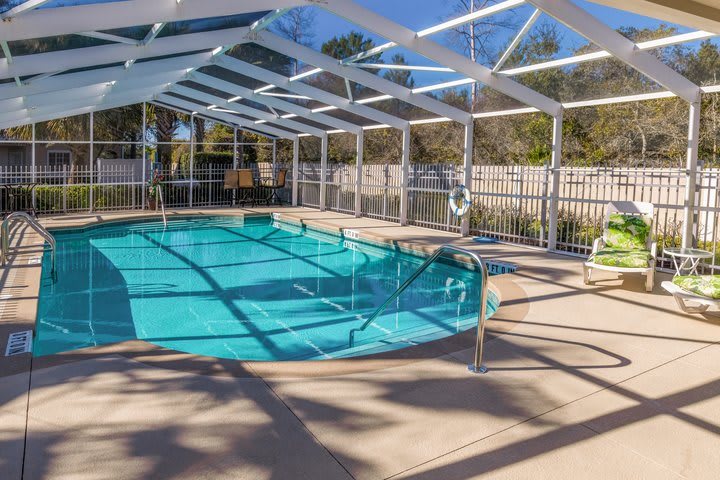 An indoor swimming pool with a transparent enclosure and a surrounding fence, illuminated by sunlight casting shadows.