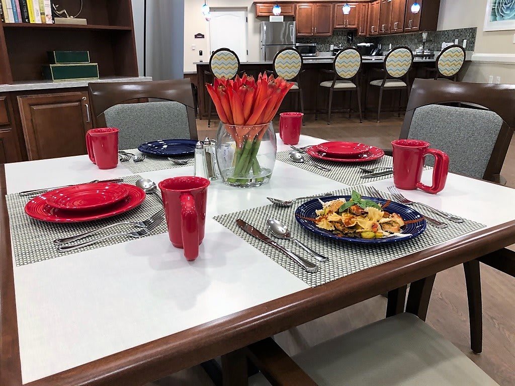 A dining table set with red and blue dinnerware, featuring a centerpiece of orange flowers.