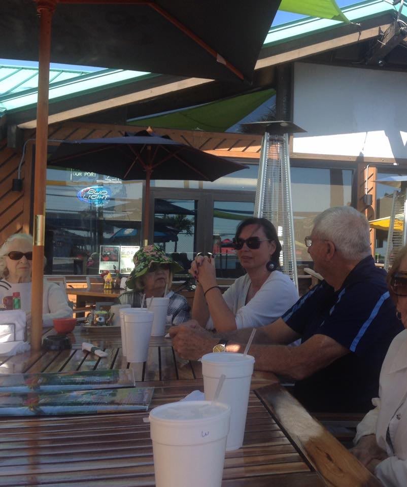 A group of people enjoying a meal together at an outdoor restaurant on a sunny day.