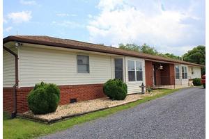 A single-story house with a combination of brick and siding exterior, featuring a driveway and landscaped bushes.