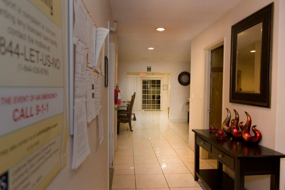 A well-lit hallway with a view of a kitchen area, featuring a table and bulletin board.
