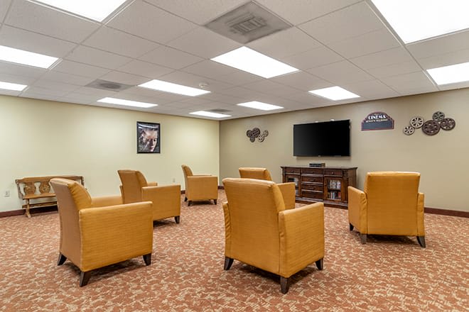 A cozy lounge area with several yellow armchairs facing a television on the wall.