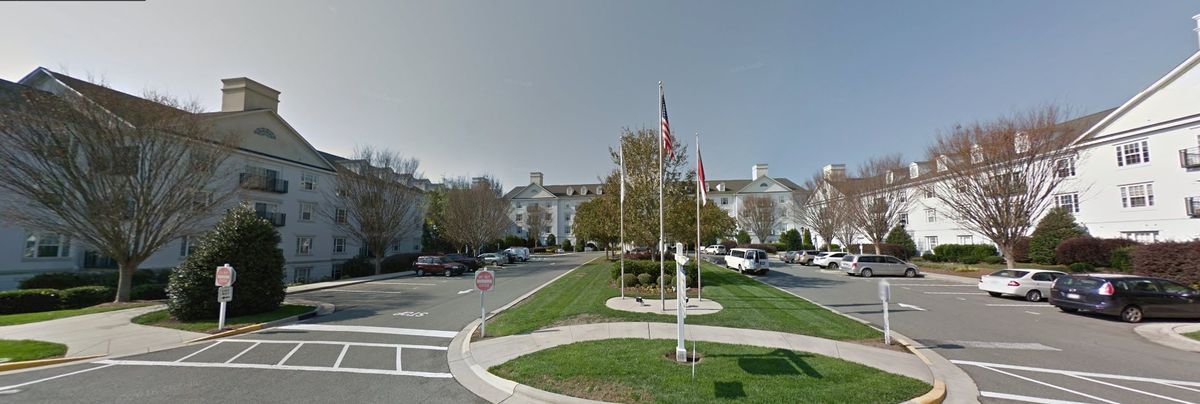 A large building with multiple floors is surrounded by a parking lot, featuring flags and trees in the foreground.