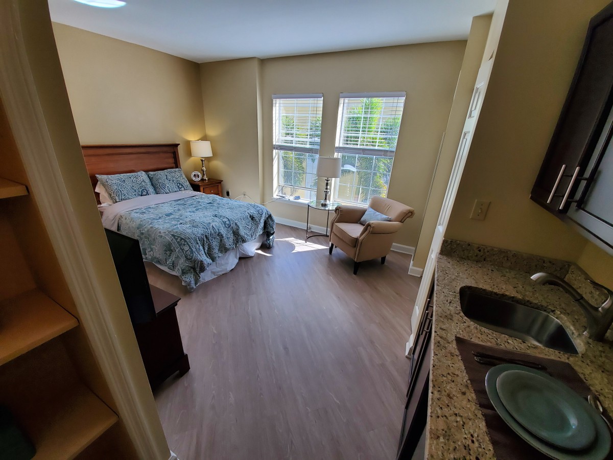 A cozy bedroom with a bed, armchair, and large windows.