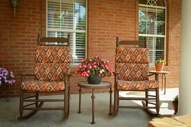 Two patterned rocking chairs on a porch with a flower pot between them.