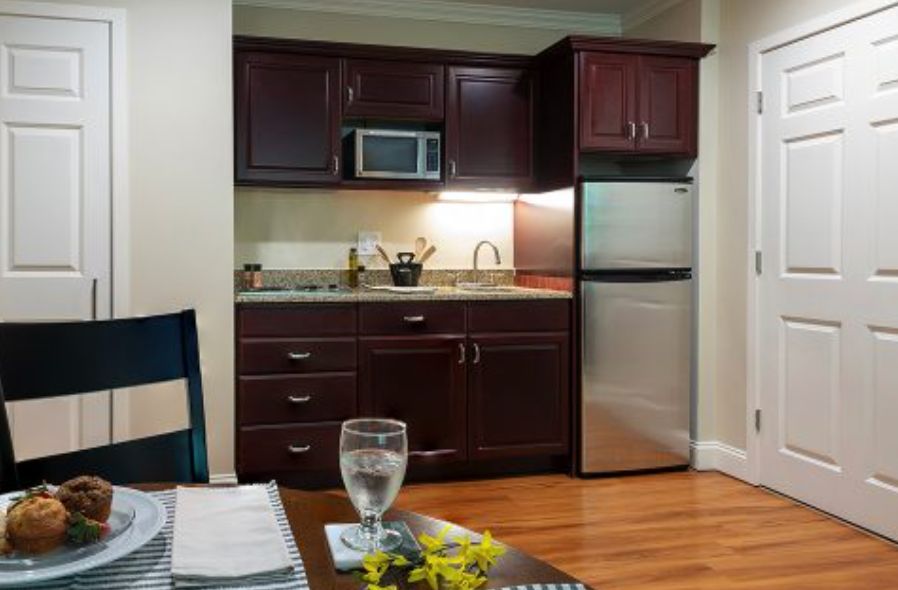 A compact kitchen setup with dark wooden cabinets, a microwave, refrigerator, sink, and countertop.