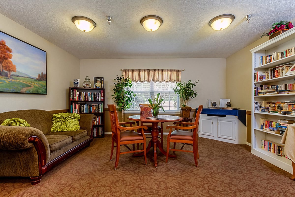 A cozy living room with a round table, chairs, and a sofa, decorated with plants and a bookshelf.