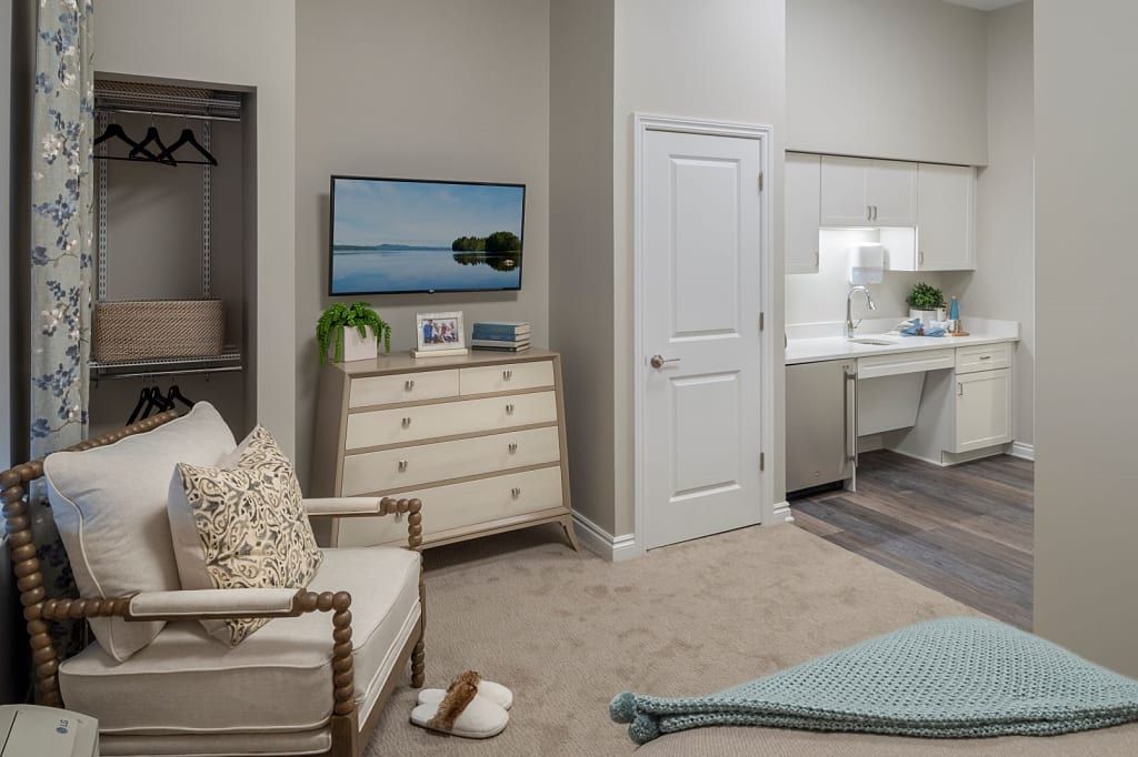 A cozy bedroom with modern furnishings, featuring a dresser with a television on top and an armchair beside it.