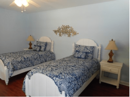 A cozy bedroom with twin beds featuring blue patterned bedding and white wooden furniture.