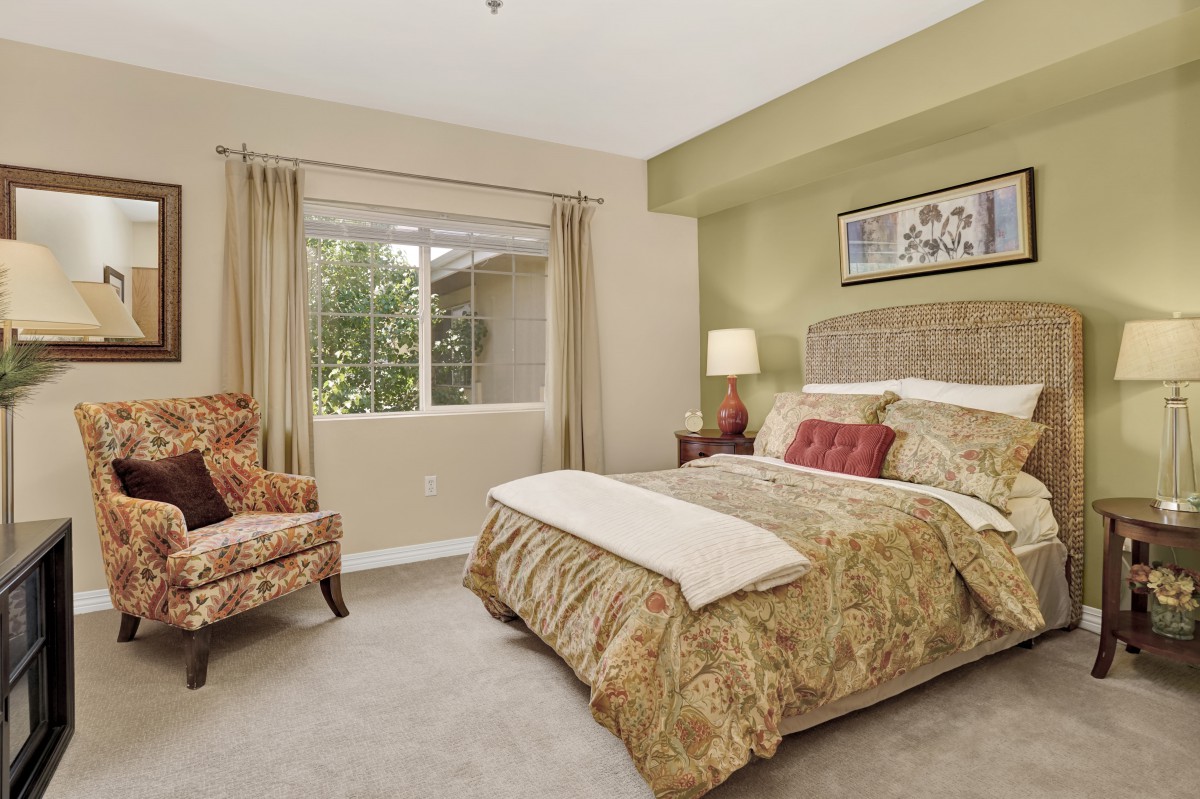 A cozy bedroom with a large bed, patterned chair, and a window with curtains.