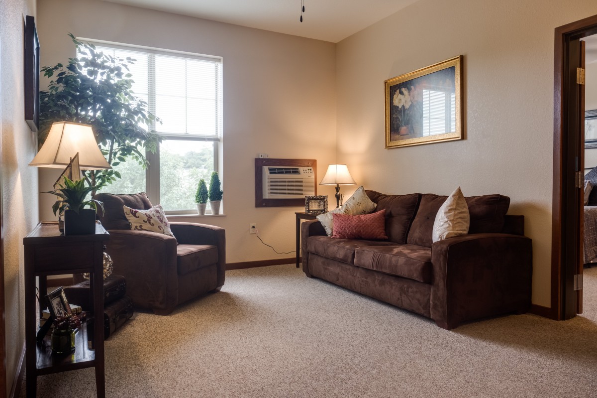 A cozy living room with a brown sofa, armchair, and a window providing natural light.