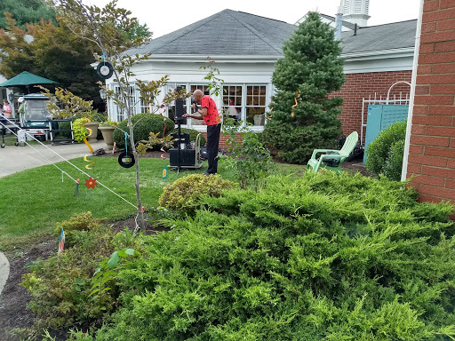 A man tends to the garden in front of a house, surrounded by lush greenery.