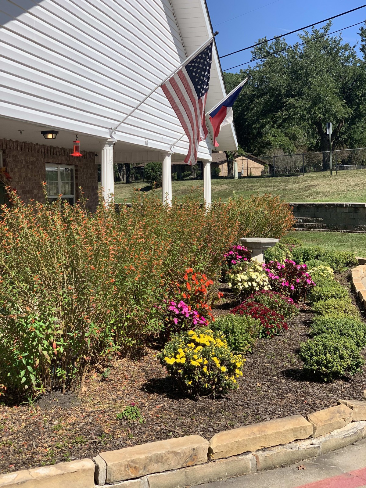 A beautifully landscaped garden with colorful flowers and flags near a house.