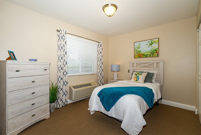 A cozy bedroom with a neatly made bed, a dresser, and decorative elements.