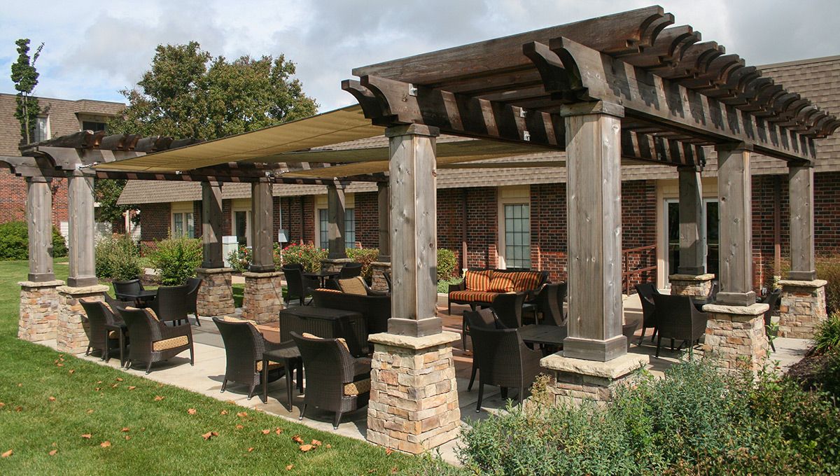 An outdoor patio with a pergola and comfortable seating, surrounded by greenery.