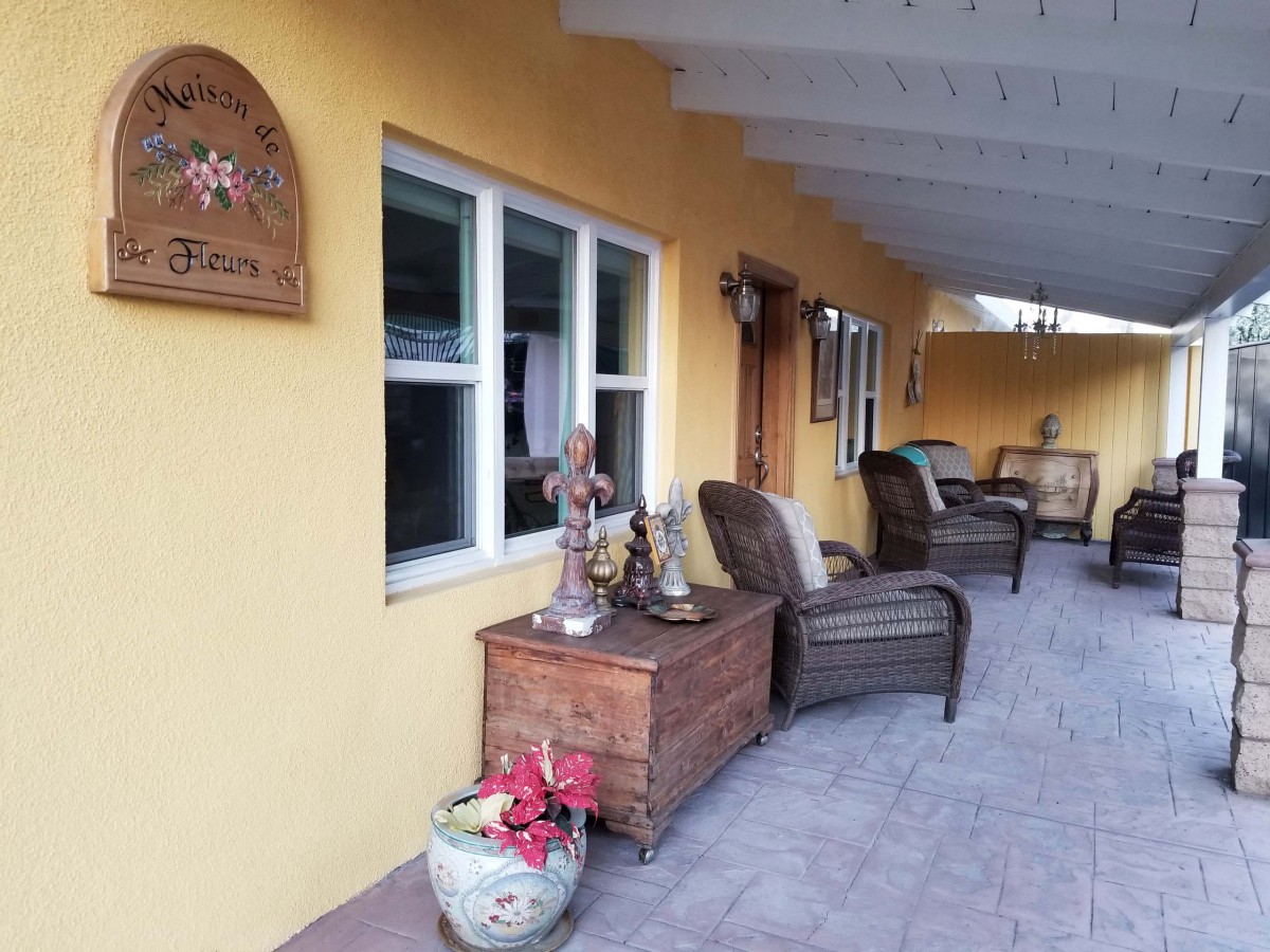 Cozy patio area with rattan chairs, decorative items, and potted plants against a yellow wall.
