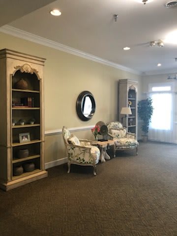 A cozy living room with elegant furniture, featuring two cushioned chairs, ornamental shelves, and a round mirror.