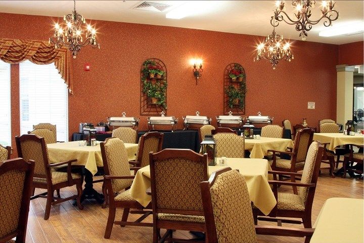An elegant dining room with chandeliers, decorated walls, and neatly arranged tables and chairs.