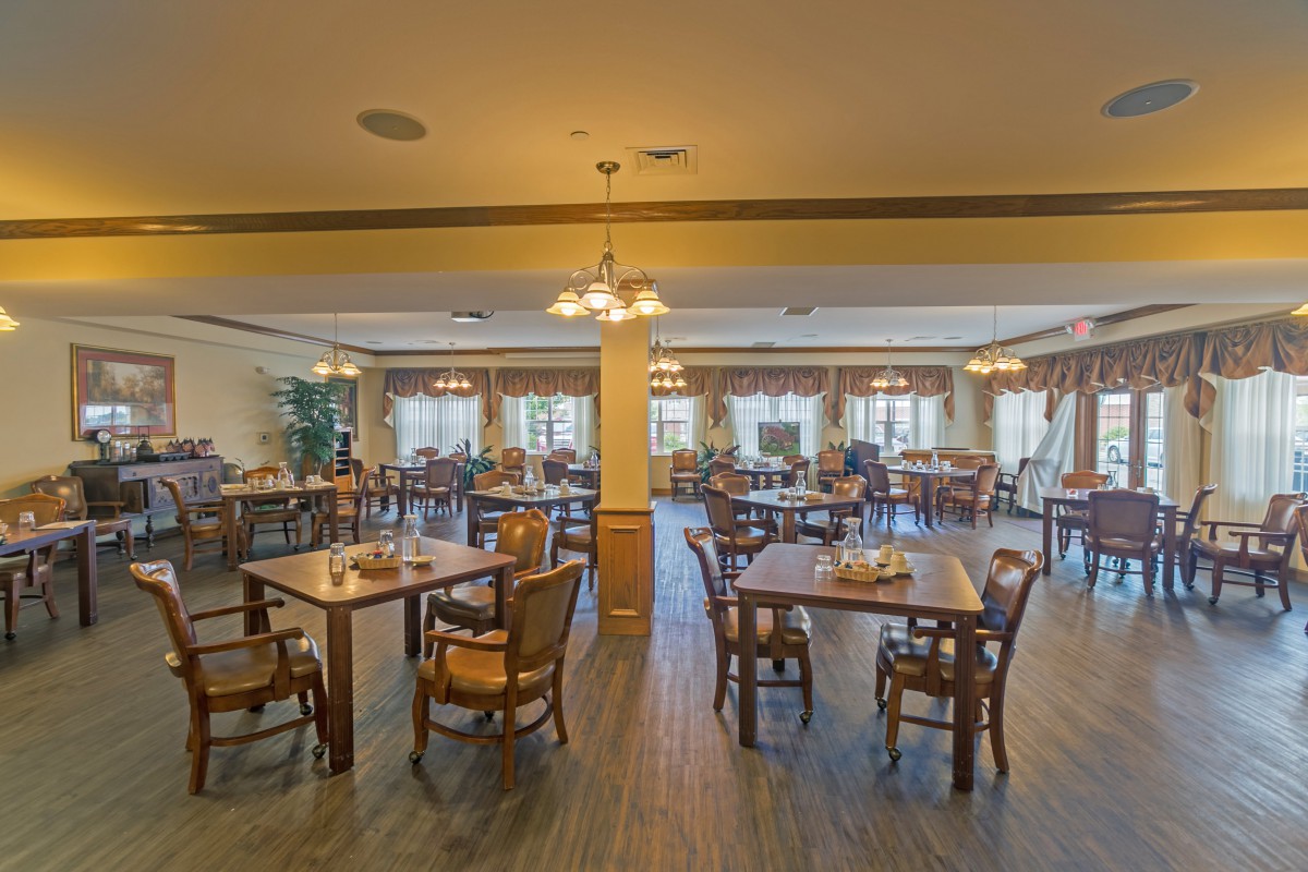 An empty dining room with neatly arranged tables and chairs, featuring warm lighting and a spacious layout.