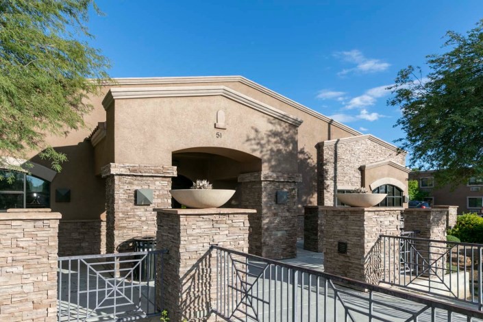 A modern residential building with a stone facade and architectural details, set against a clear blue sky.