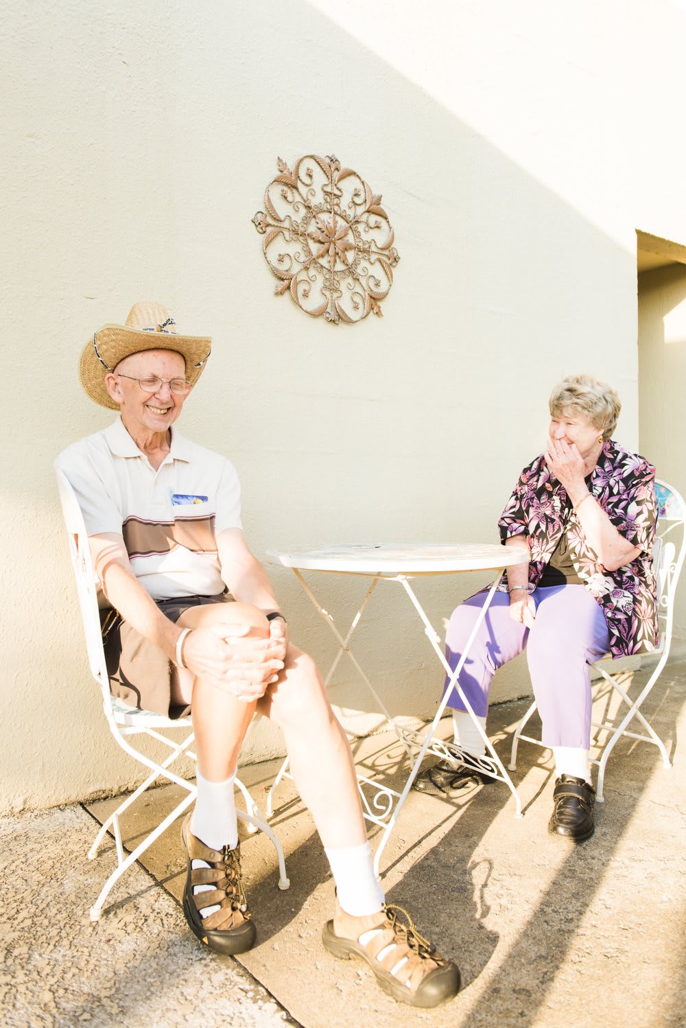 An elderly couple enjoying a conversation outdoors at a small table.