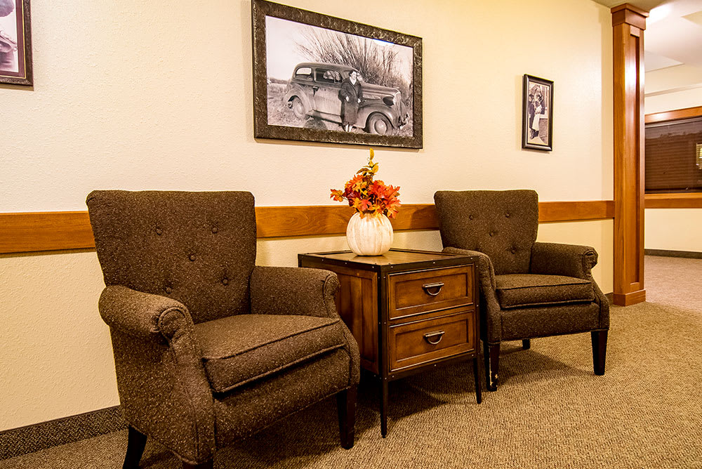 A cozy lounge area with two brown armchairs, a wooden side table, and vintage photographs on the wall.
