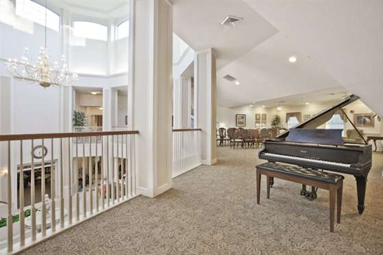 A bright and spacious interior with a grand piano, carpeted floors, and an elegant railing.