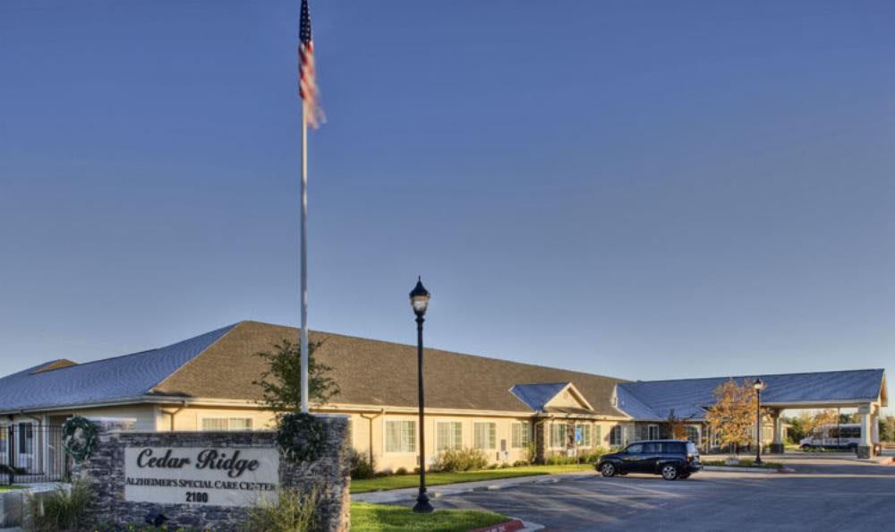 A building with a sign and an American flag in front, alongside a vehicle parked nearby.