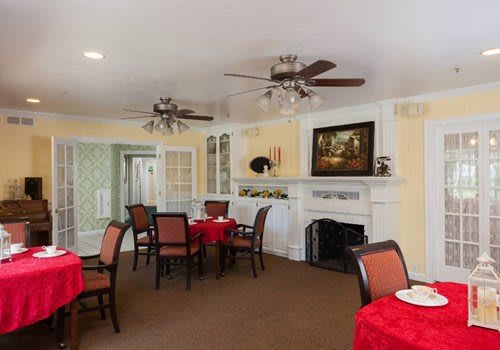 A cozy dining room with red tablecloths, ceiling fans, and a fireplace.