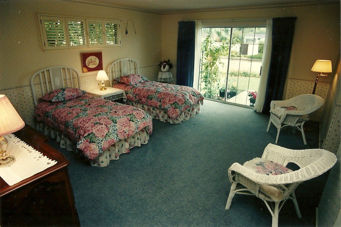 A cozy bedroom featuring twin beds with floral bedding, a nightstand with a lamp, and a sliding glass door leading outside.