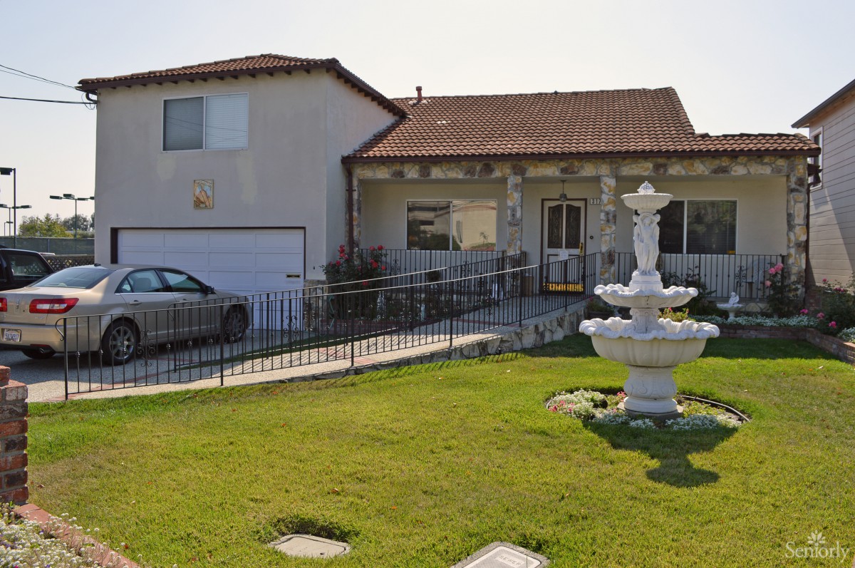 A two-story house with a front lawn and fountain, featuring a driveway with a parked car.