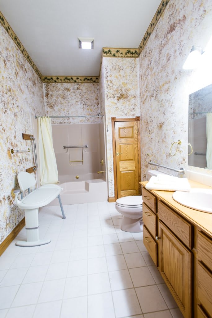 A vintage-style bathroom with wooden cabinetry and floral wallpaper.