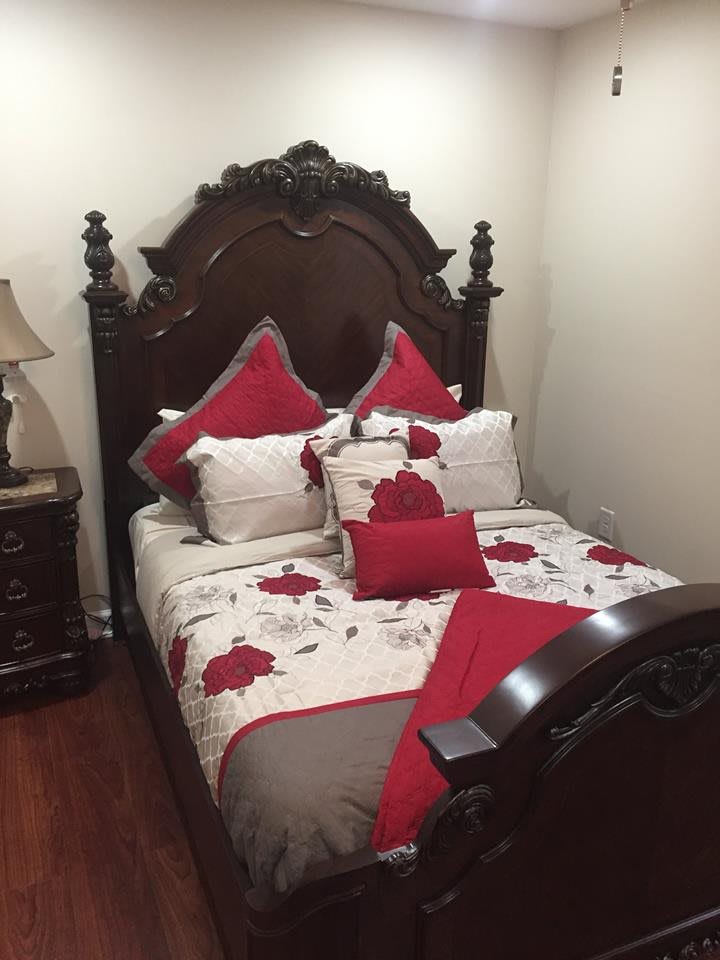 A cozy bedroom with a bed featuring red and white floral bedding and an ornate wooden headboard.