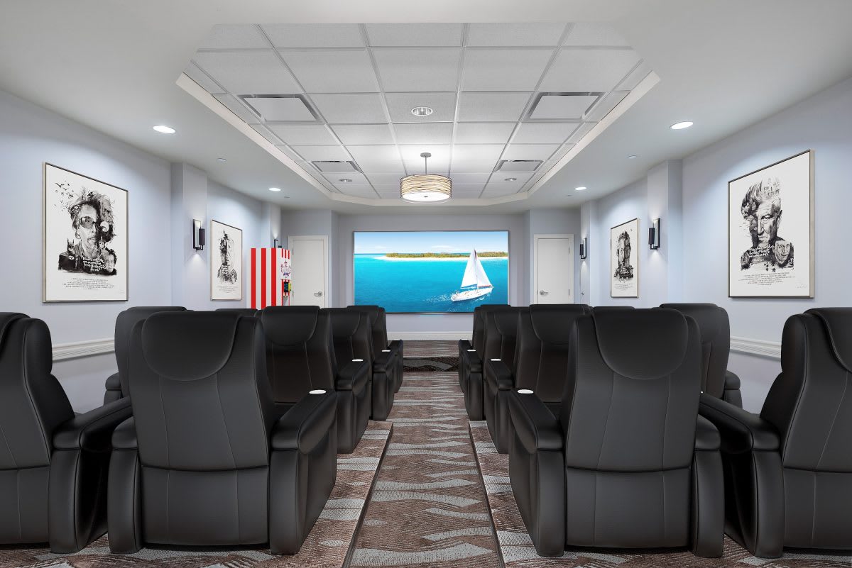 A modern theater room with rows of black leather chairs facing a large screen displaying a sailboat scene.