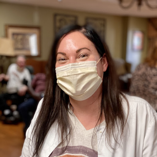 A smiling person wearing a mask in a lively indoor setting.
