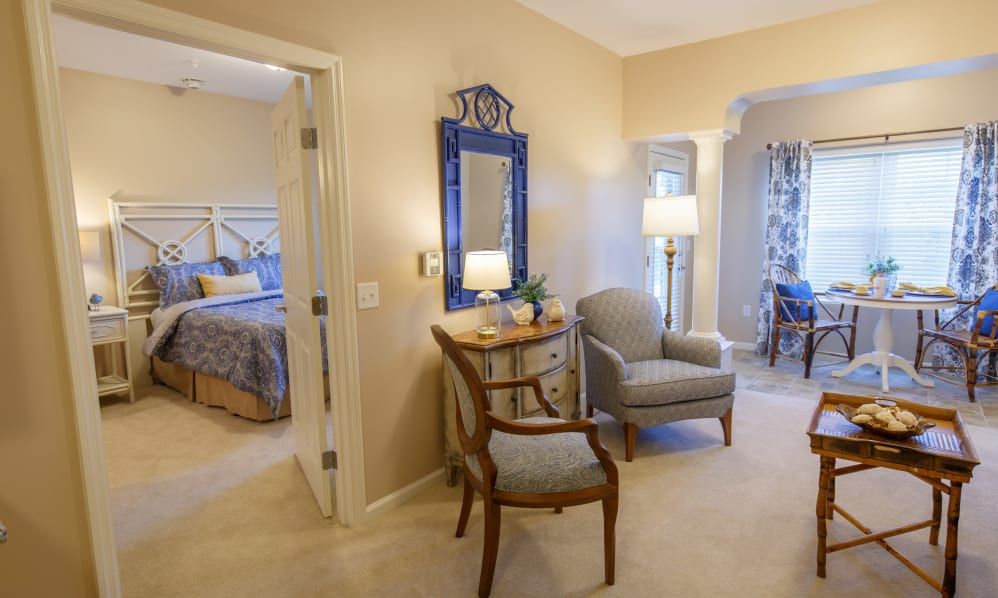 A cozy living area with chairs, a lamp, and decorative mirror leading to a bedroom.