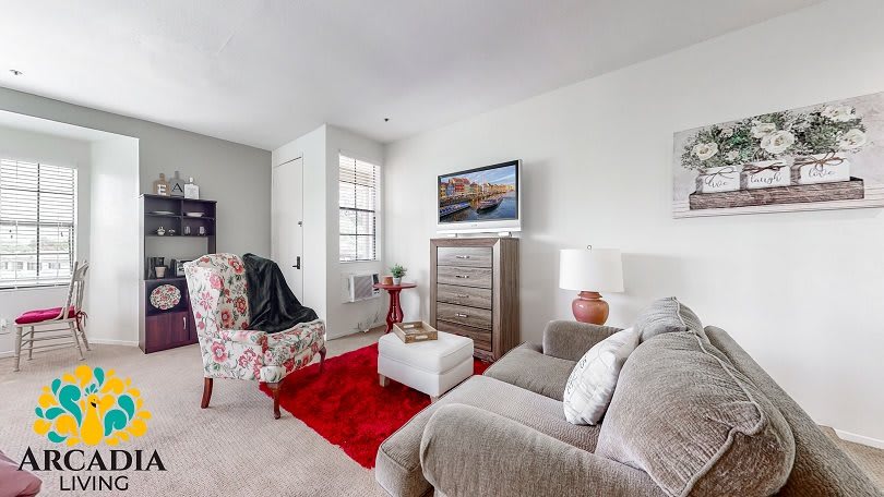 A cozy living room with a sofa, floral armchair, and a red rug, featuring a wall-mounted television and stylish decor.